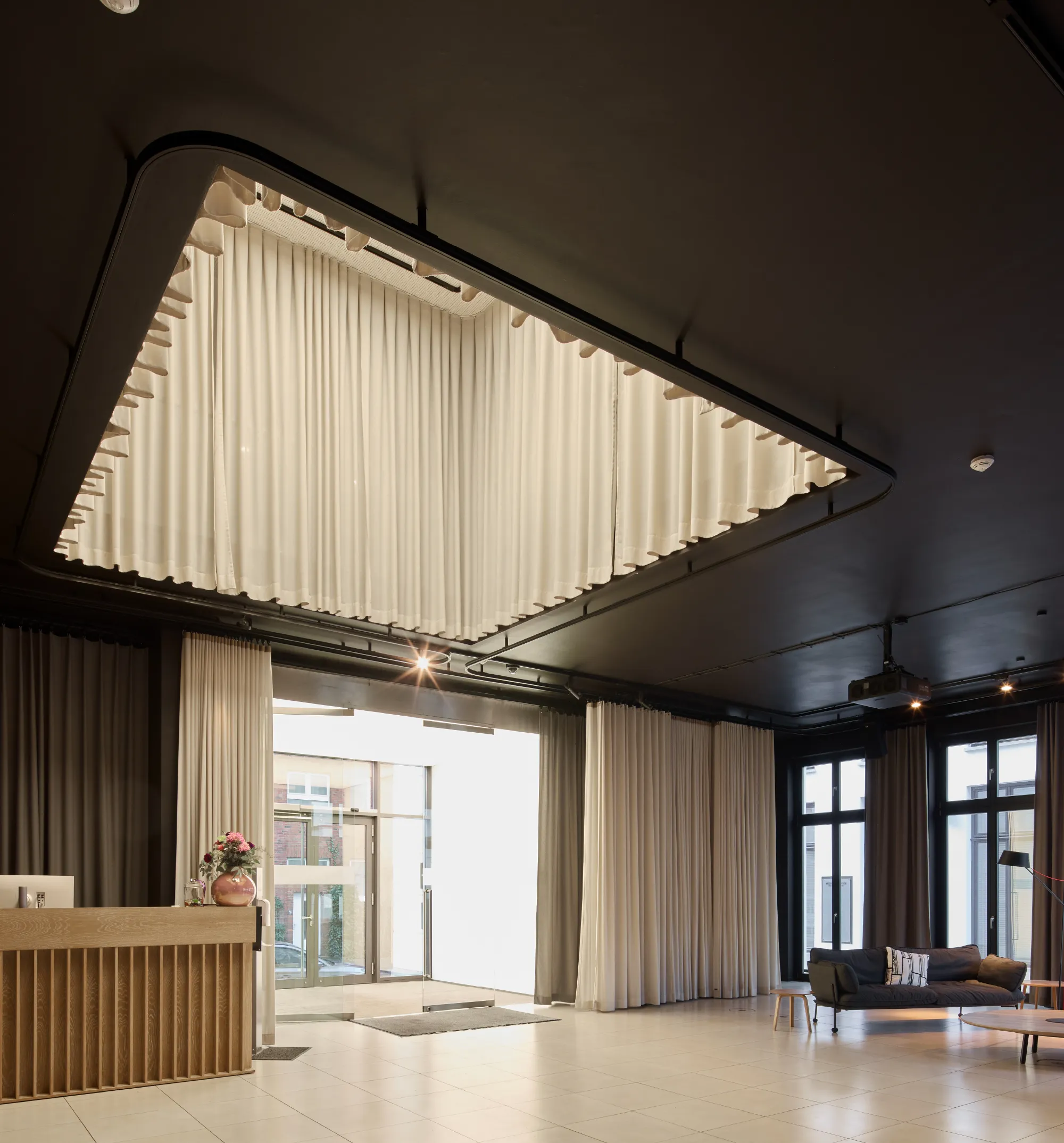 Ein modern gestalteter Empfangsbereich mit einem eleganten Deckenelement und hellen Vorhängen schafft eine einladende Atmosphäre.